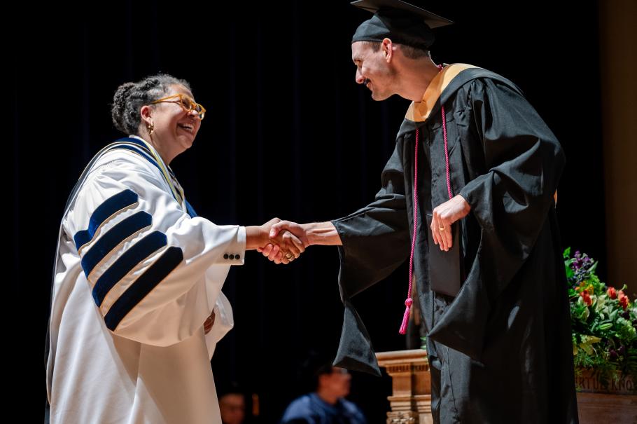 Smith President Sarah Willie LeBreton wearing white academic robes shakes the hand of a graduate