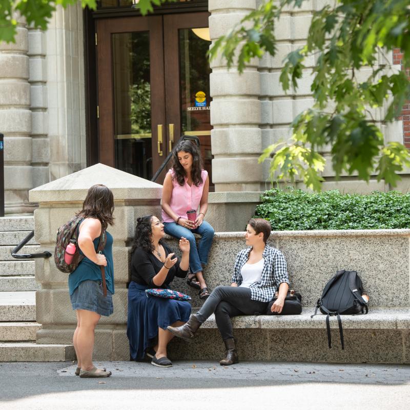 A group of students sits outside Seelye Hall. They are engaged in conversation with one another. 