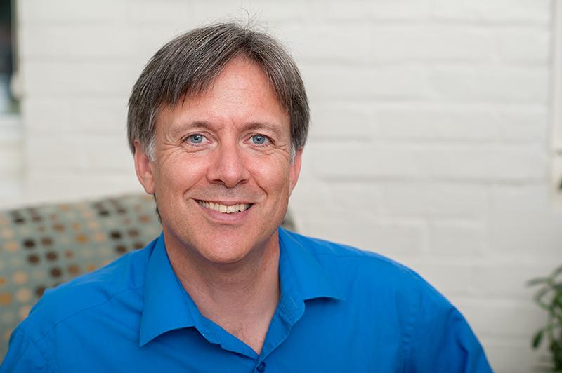 Instructor stephen bradley smiles in front of a white brick wall in a blue collared shirt