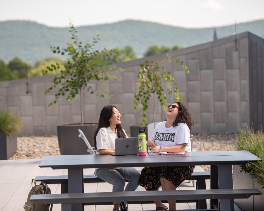 Two students sit at a picnic table on the rooftop terrace of Neilson Library.