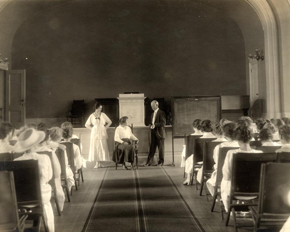 A archival photo of an auditorium filled with students in white nursing dresses.