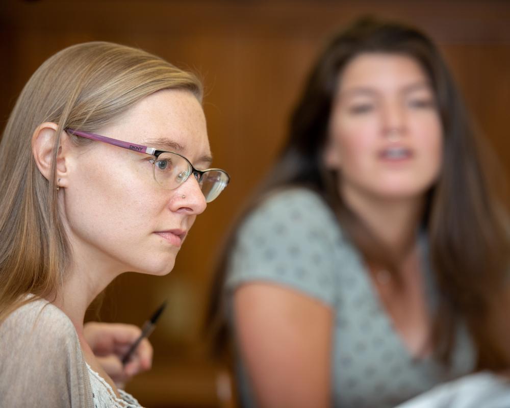 A student listens carefully as someone else speaks. In the background, another student looks on. 