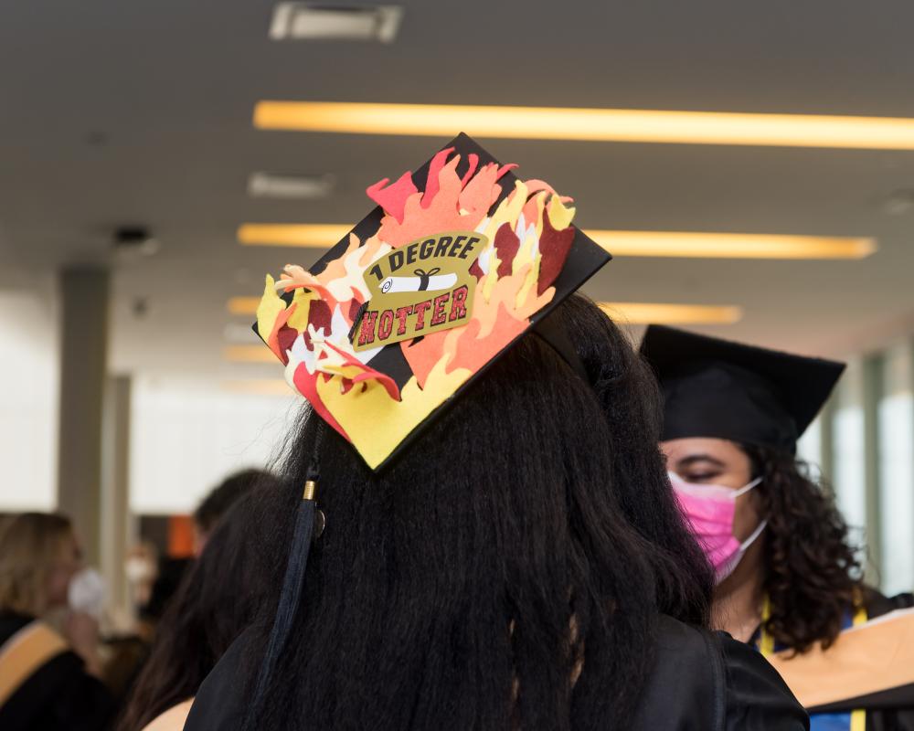 A photo of the cap of a student who has decorated their cap with the words "1 degree hotter" and flames.