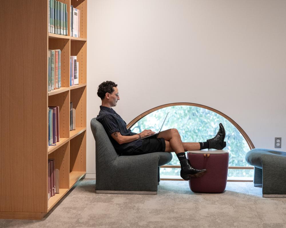 A student sits in profile in front of an arched window in the library