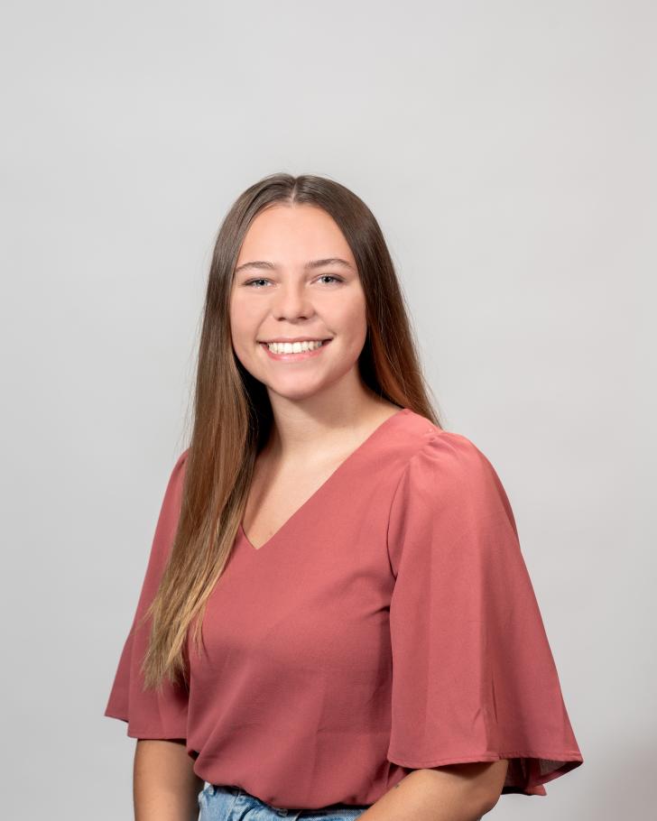 Molly Vencel wears a coral shirt and smiles at the camera. 