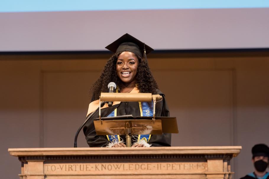 Beth Nanjala Luvisia wears a cap and gown as she stands behind the podium delivering a speech during Commencement 2022.