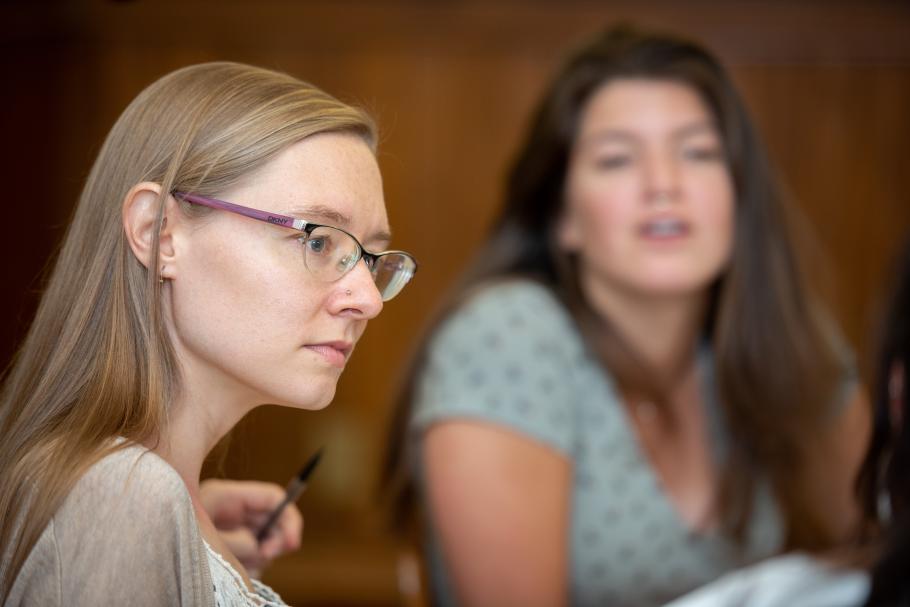 A student listens carefully as someone else speaks. In the background, another student looks on. 