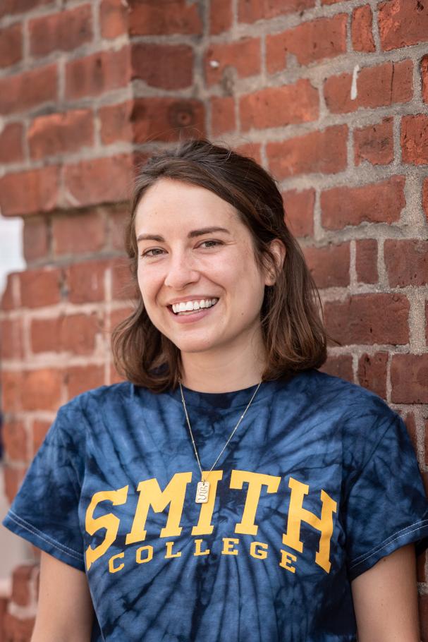 Eve White stands in front of a brick wall wearing a tie-dyed Smith College t-shirt.