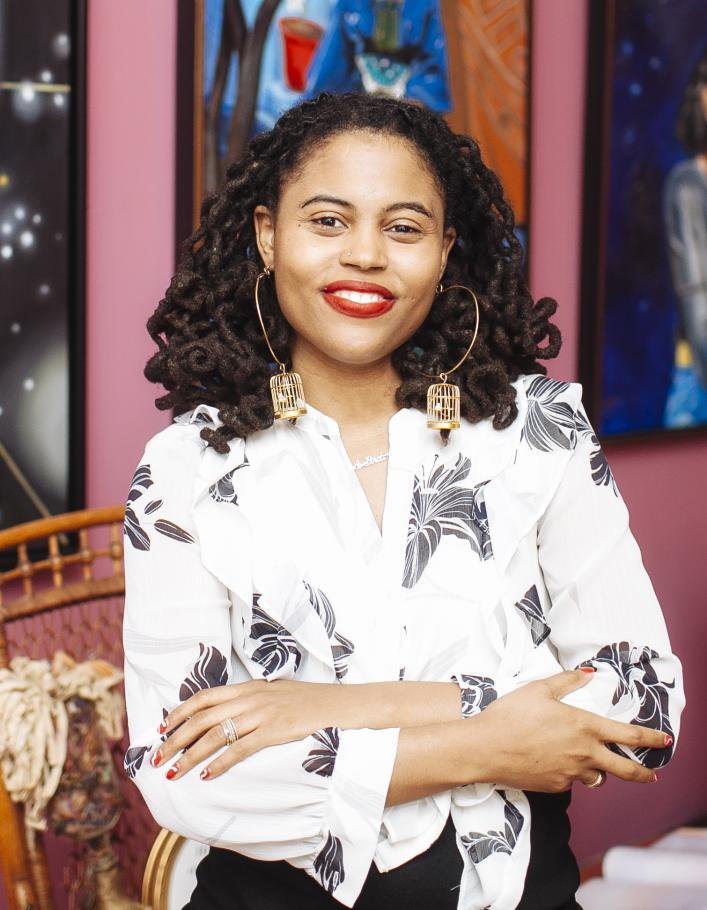 Loren Cahill stands in the Colored Girls Museum in Philadelphia wearing a black and white blouse. Her arms are folded in front of her.