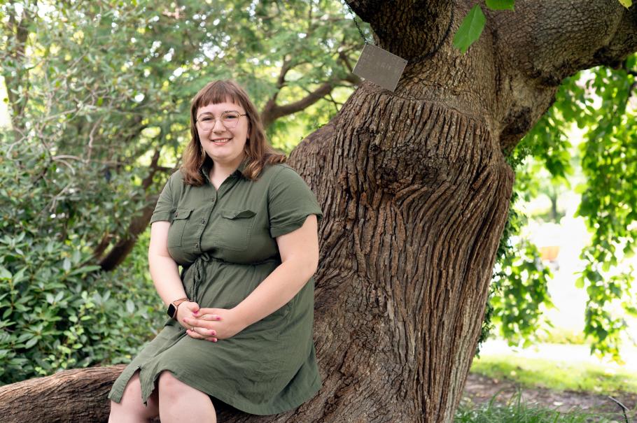 Kyleigh Murchison sits on a tree trunk surrounded by greenery. 