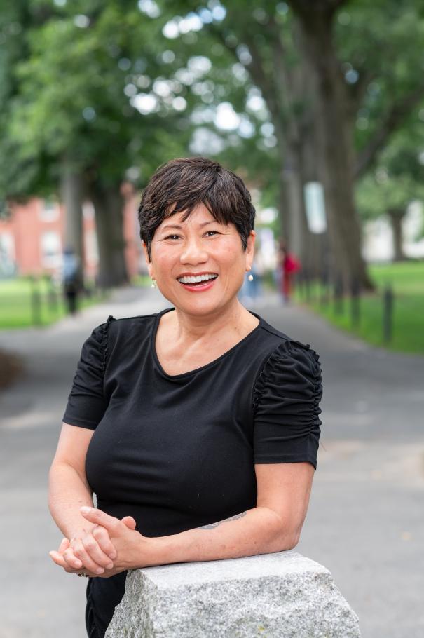 Dean Marianne Yoshioka leans against a stone pillar wearing a black dress.