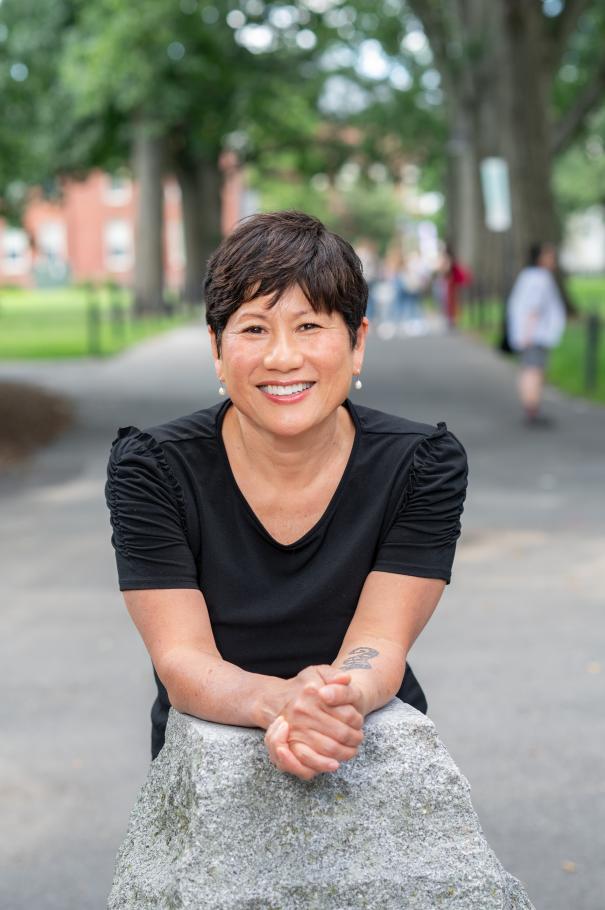 Dean Marianne Yoshioka leans over as stone pillar wearing a black dress.