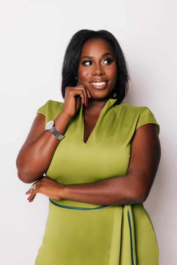 Deran Young looks to the side and smiles wearing a green wrap dress. 