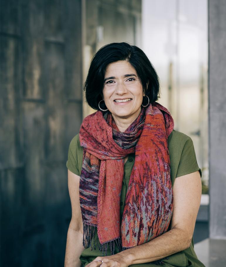 instructor ann augustine, wearing a multi-colored red amd blue and purple scarf, smiles in front of a wall