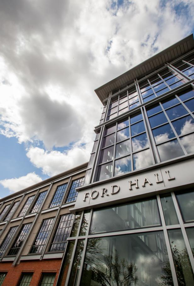 Ford Hall, a glass and brick building with clouds and sunshine and the words "Ford Hall" in letters