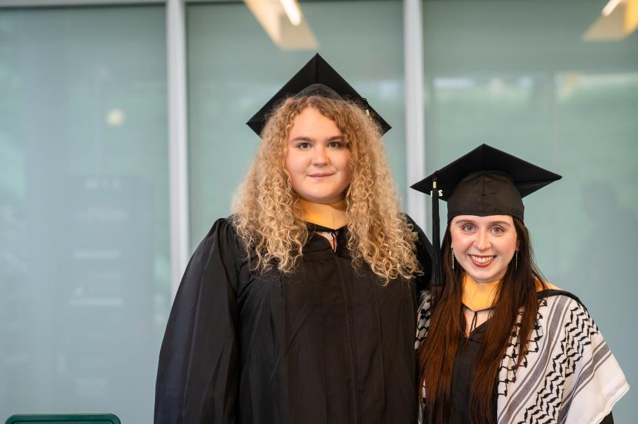 Taylor McCain and Isabelle Brown, wearing black academic robes and mortarboards stand together smiling