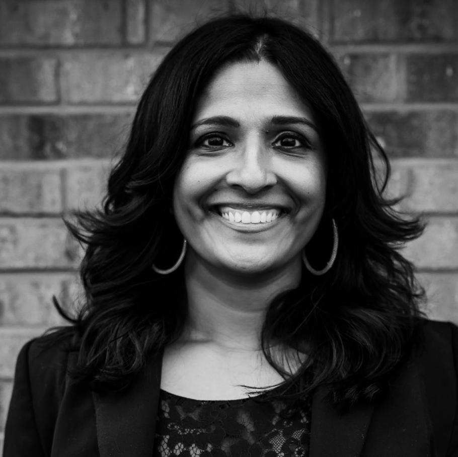 Rani Varghese in black and white photo smiles with brick wall behind