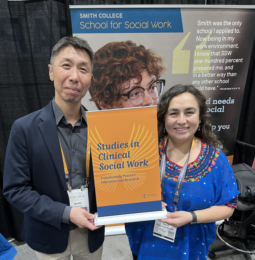 Kenta Asakura and Maria Ximena Maldonado-Morales stand holding a small poster that is orange with blue text that reads Studies in Clinical Social Work