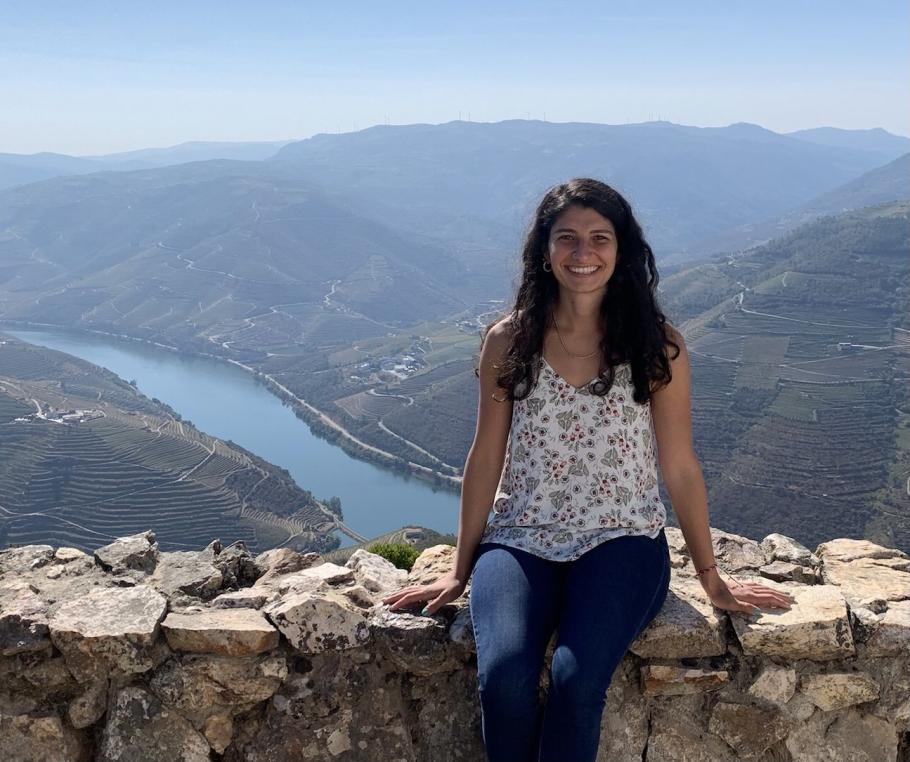 Kristina Domaney sits on a stone wall with a lake and mountains behind