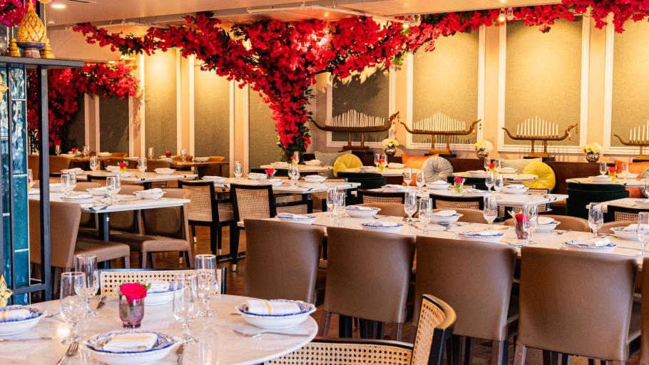 A dining room with white walls, tan chairs, and red bougainvilla flowers arching above the table