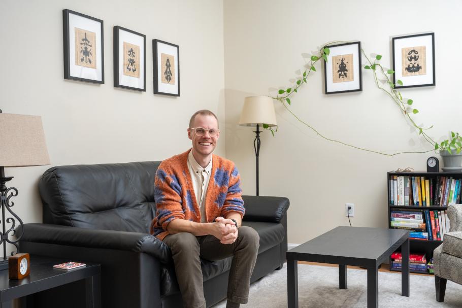 Kai Pratt poses in an office with a black couch, black bookshelf and black coffee table.