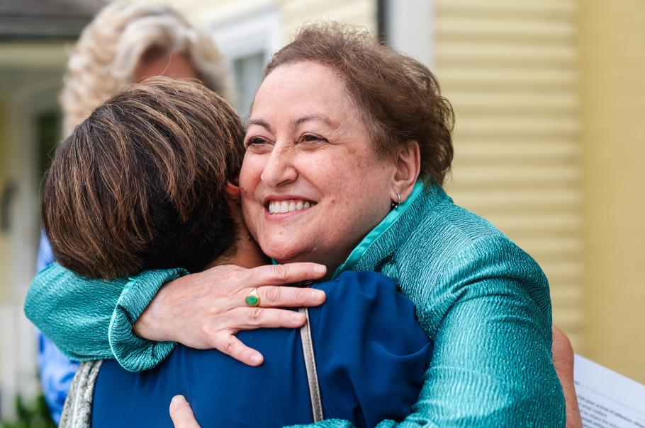 Yvette Colon hugs Dean Marianne Yoshioka in front of a yellow building