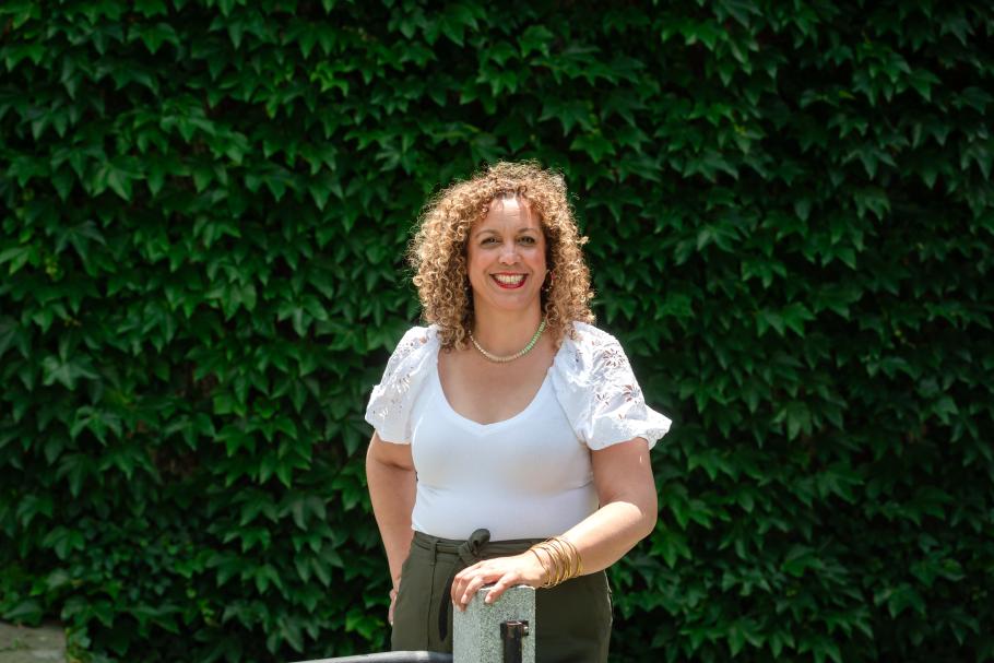 Simone Jacobs wearing a white blouse stands in front of a wall of green leaves