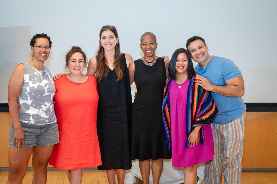 Six doctoral students stand next to each other, smiling with arms around each other.