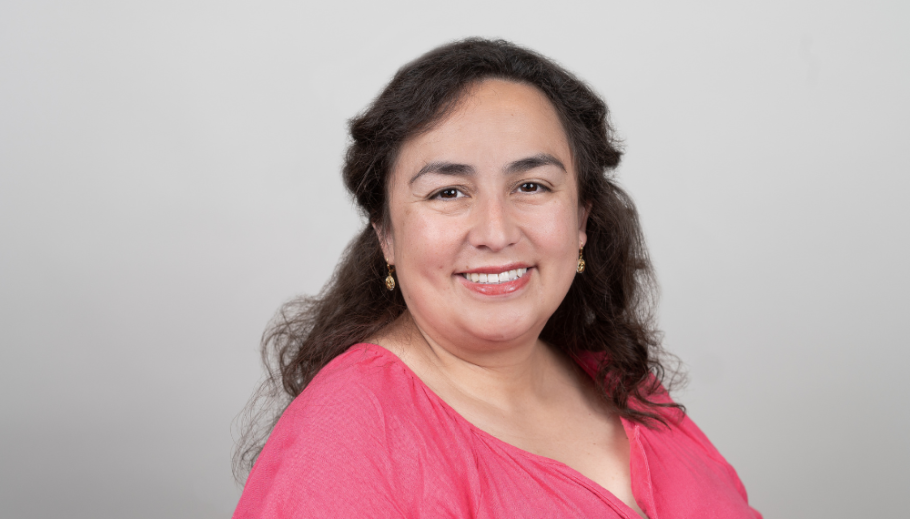 Maria Maldonado-Morales wearing bright pink shirt against grey wall smiling