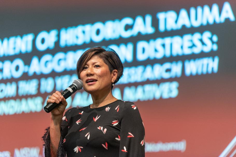 Marianne Yoshioka speaking at Public Lecture Series 2018 holding a mic with screen behind