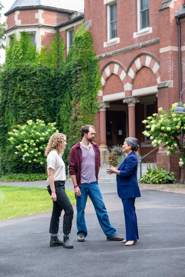  Dean Yoshioka chats with 2025 graduates Iain Cooley and Isabel Snodgrass outside brick buildings