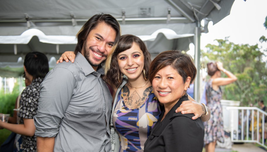 Marianne Yoshioka stands with two graduates with arms around each other