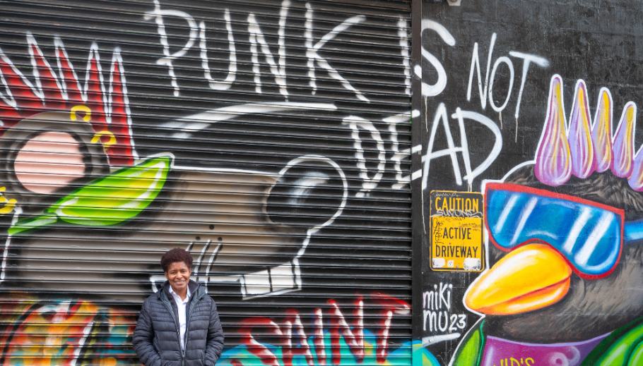 JD Fuller stands in front of a spray painted mural of a rat and penguin with mohawks that reads Punk is Not Dead