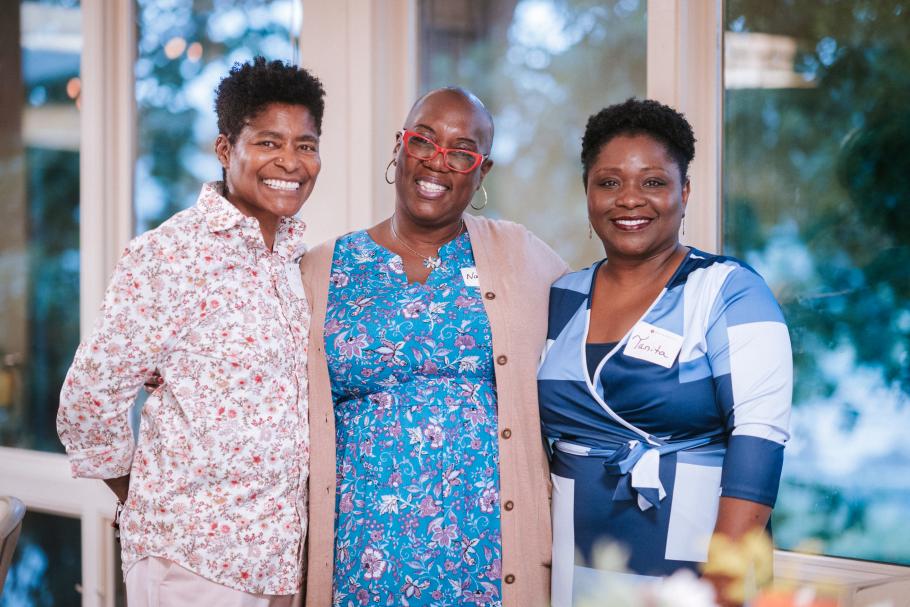 JD Fuller stands with two alumni during the 2025 Alumni Awards. Tall windows behind