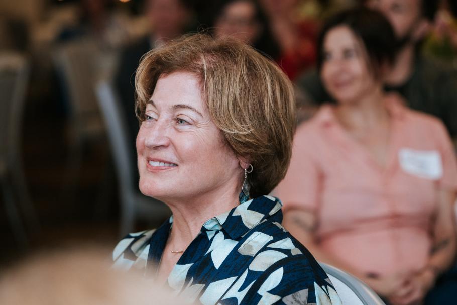 Laurie Peter sits at alumni award ceremony 2025 with people sitting in background