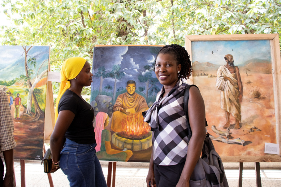 Student and Fidelis Nabukenya (r) at Uganda Narratives Conference with art behind- organized by Hugo Kamya