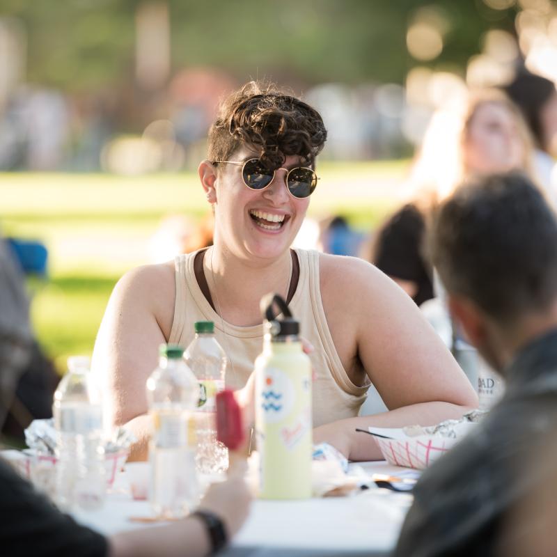 A student sits at a table laughing with other students during the SSW opening weekend dinner.