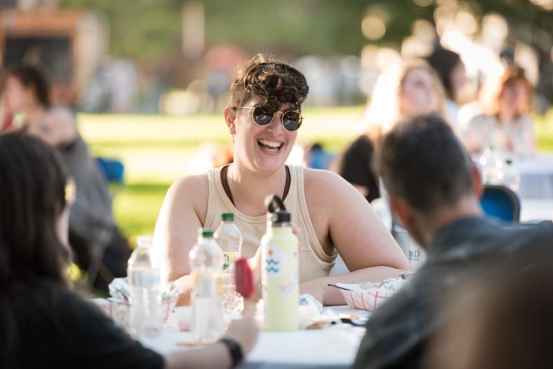 A student sits at a table laughing with other students during the SSW opening weekend dinner.
