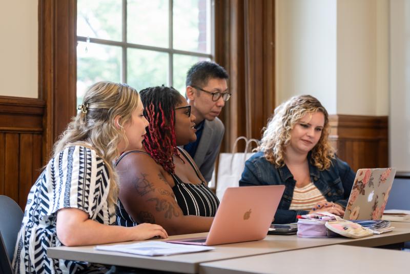 Three students work with a professor in the classroom.