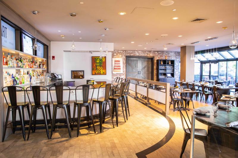 A photo of the interior of ArtBar Cambridge. A bar with high top chairs is visible on the left, the right features high top tables.