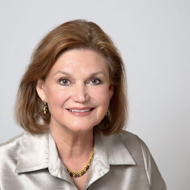 Instructor Gianotti sits in front of a gray background in a shimmering silver blouse, smiling forwards