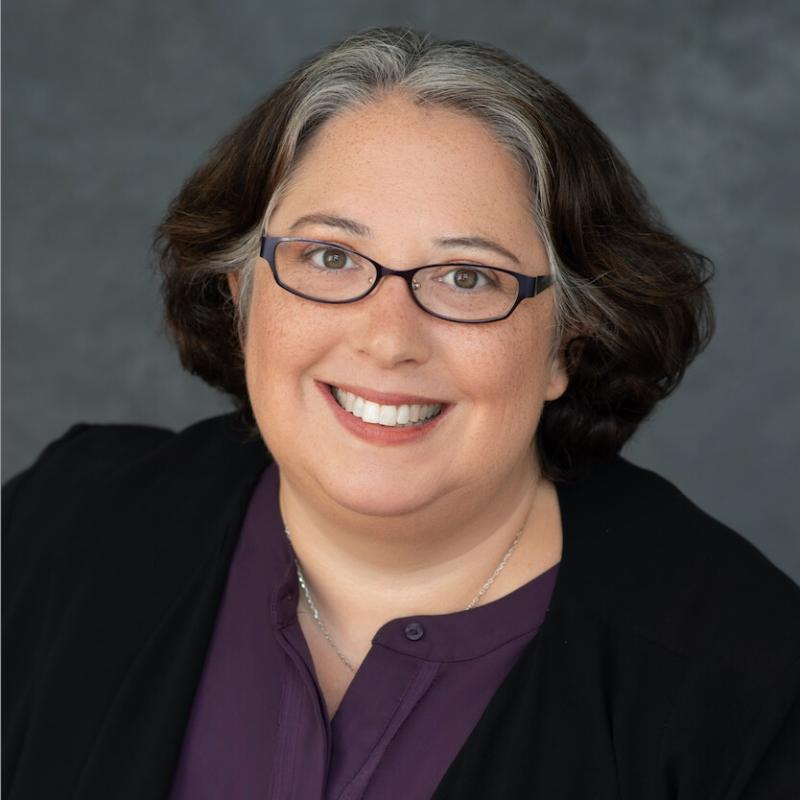 Instructor Bogin smiles forward in glasses, wearing a dark jacket over a purple blouse