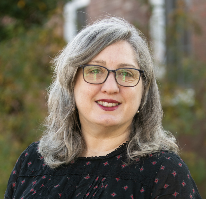 instructor slayter elspeth wears dark-rimmed eyeglasses, a dark shirt and smiles forward