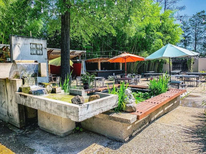 A patio with cement fountain and cafe umbrellas, tables, trees