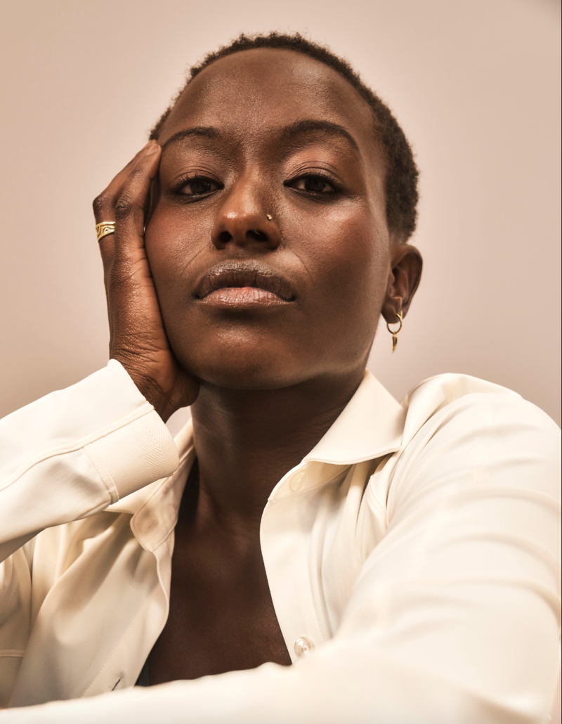 Oumou Sylla, a person with short dark hair wearing a white collared shirt with their hand on the side of their face