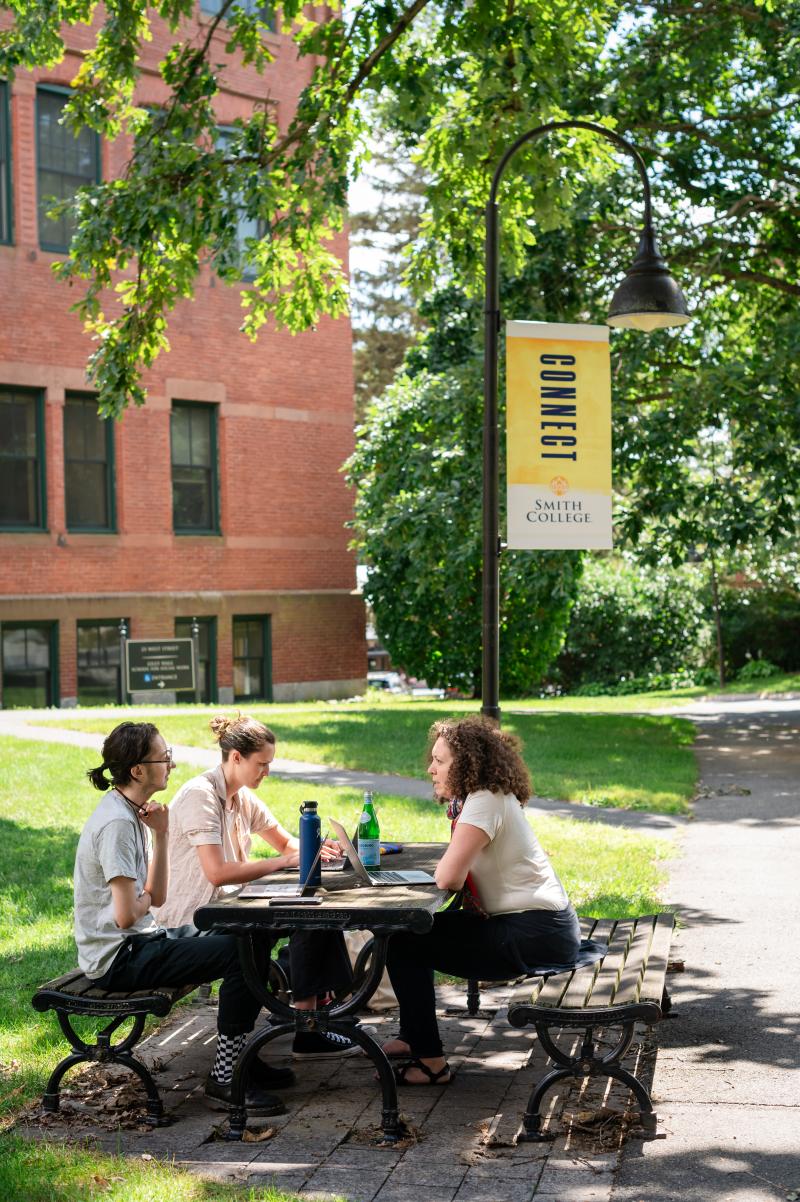 Three students sit at a picnic table on the Smith College campus.