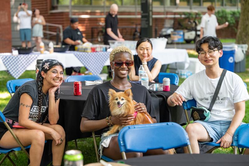 Four students sit at a table outside, person in center is holding a small tan pomeranian dog