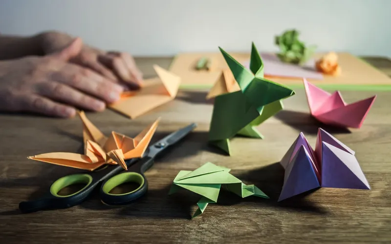 a wooden table with scissors and origami art and hands in the background resting on the table