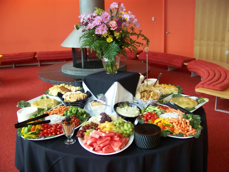 A table coveered with flowers and trays of charcuterie, fruit, and vegetables. 