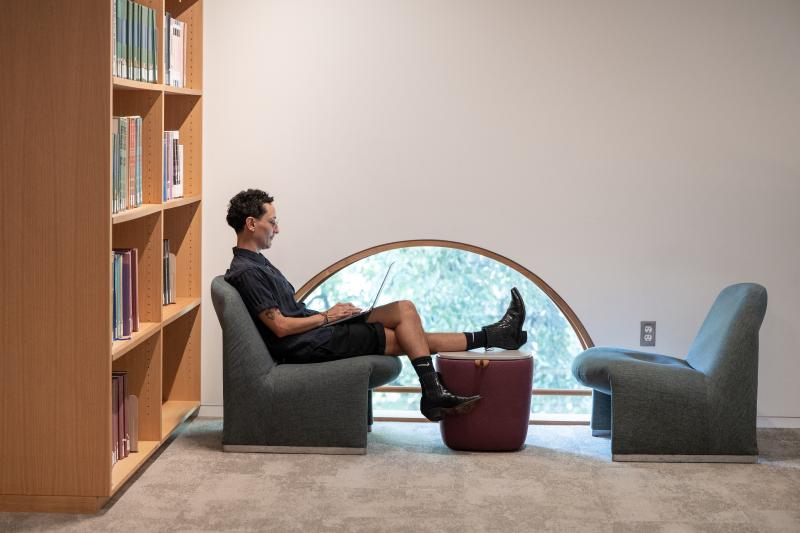 A student sits in profile in front of an arched window in the library